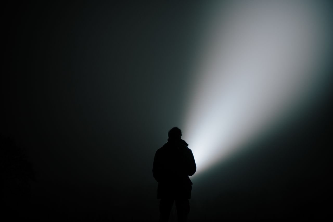 A silhouetted person shines a light into a foggy dark space