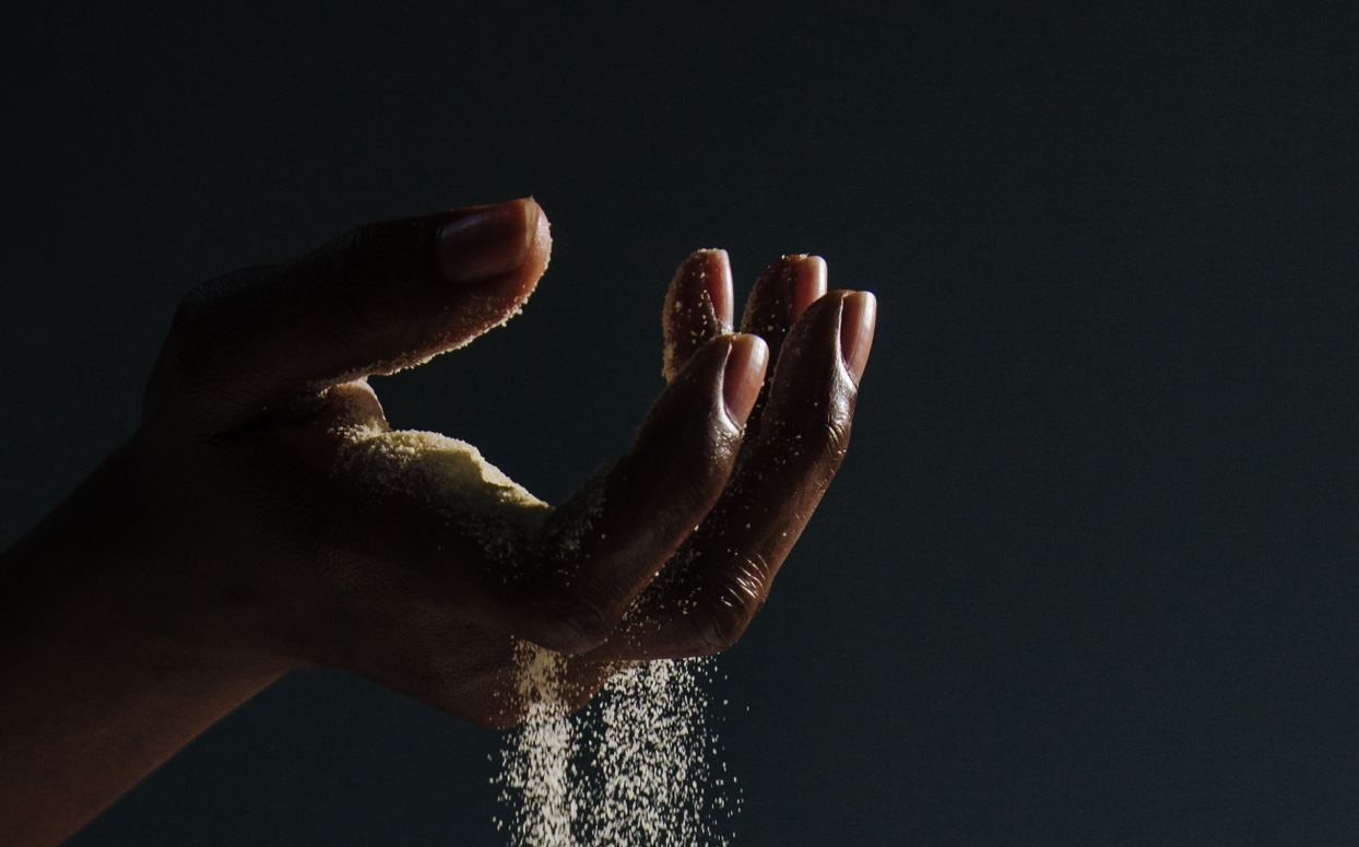 Sand falls through a person's fingers.