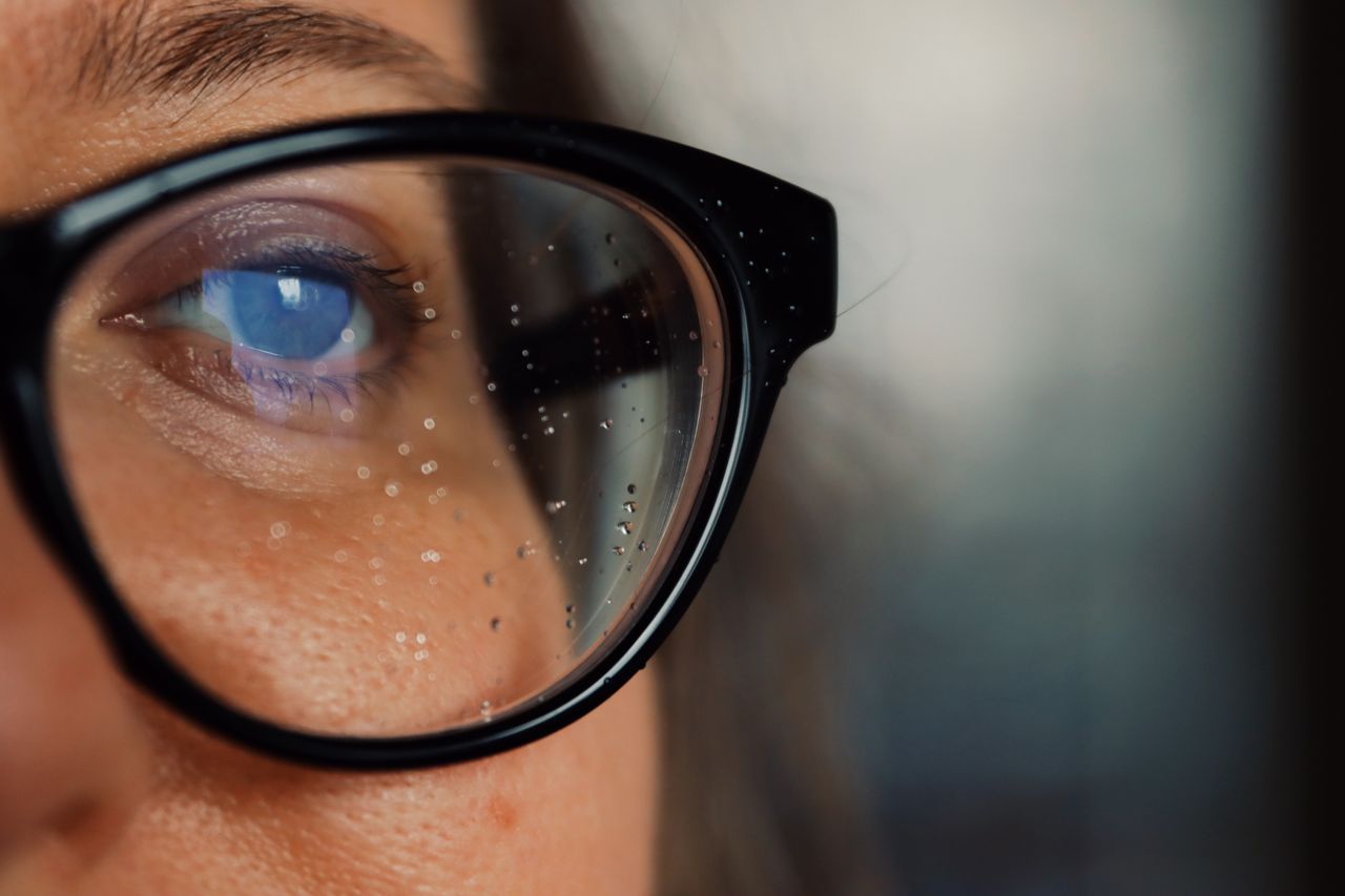 A person looks out through glasses speckled with water droplets